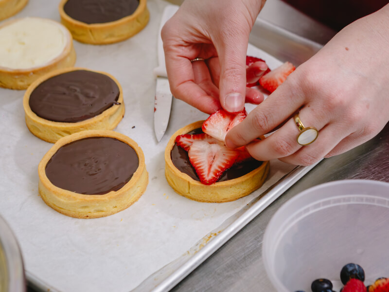 Hands placing strawberries on chocolate tarts in a baking class